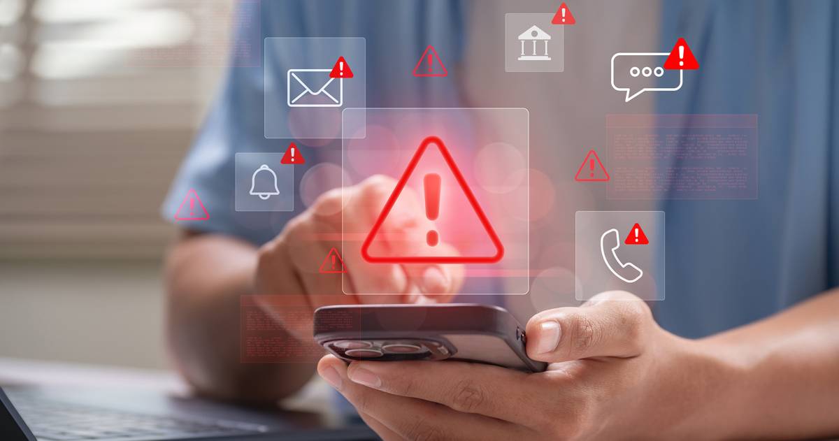 Man achter laptop met telefoon in de hand waarop allerlei phising meldingen gegeven worden