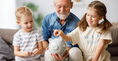 Een opa helpt twee kinderen met sparen en doet muntjes geld in een spaarvarken